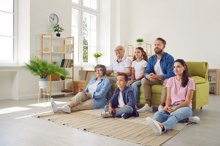 Happy big family enjoying weekend together at home. Multi-generational family gathered together at home to watch their favorite TV show. Small, adults and old family members sitting in front of TV.の写真素材