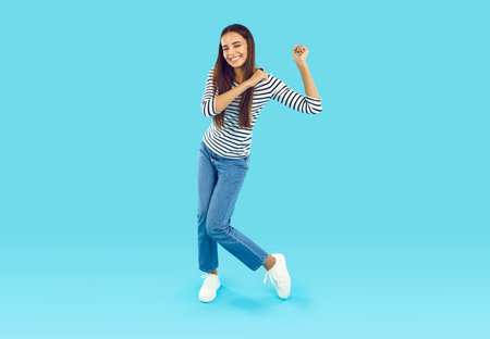 Full size photo of a happy young brunette with straight long hair in a striped sweatshirt and blue...