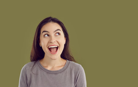 Photo of amazed excited girl with opened mouth. Surprised brunette girl looking up to side with copy...