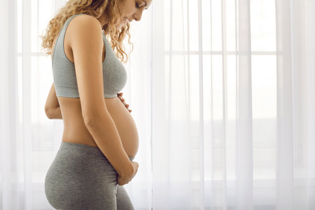 Crop of healthy sporty young pregnant woman in sportswear touch big belly await for newborn baby...
