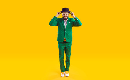 Full body shot of happy cheerful joyful funny smiling handsome bearded man wearing green suit and black hat standing on yellow studio background. Fashion and St Patricks Day conceptの写真素材