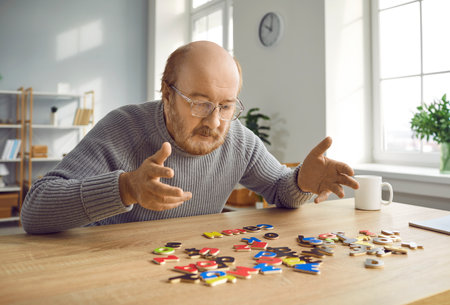 Senior man with dementia doing puzzles as a brain and memory training activity. Old bald bearded man in glasses sitting at a table and making up words with alphabet letters Alzheimers disease conceptの写真素材