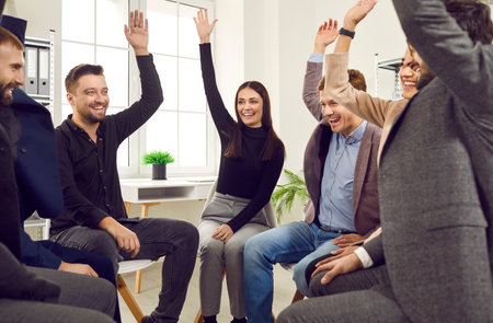 Happy business team having fun in the office. Group of cheerful young people sitting in a circle, giving each other a high five or raising hands up and voting for a good suggestion. Teamwork conceptの写真素材