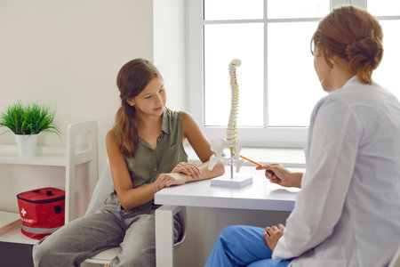 Preteen girl listens to lecture from doctor about structure of spinal human vertebrae at orthopedic...