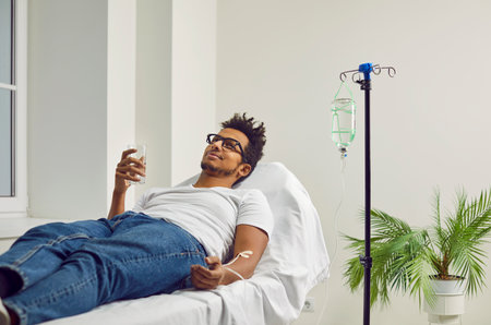 African American man getting treatment at the clinic or hospital, lying on a medical bed, receiving...