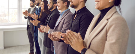 Happy audience applauding speaker at business conference or corporate team meeting. Group of people in formal suits standing in row in office, clapping hands and smiling. Banner, header backgroundの写真素材