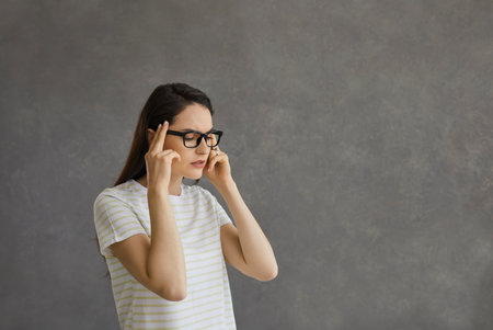 Serious young woman in glasses with eyes closed trying to calm down, relax, cope with stress,...
