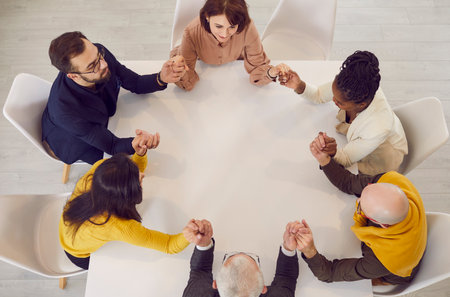 Team of business people sitting around table holding hands. View from above of male and female colleagues sitting closed together at office table at corporate meeting. Unity, support, conceptの写真素材