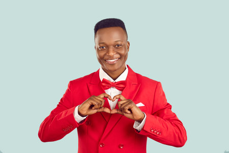 Handsome adult Afro American man in red suit makes hand heart shape. Benevolent human gentleman philanthropist businessman benefactor charity fund founder donates money wishes healthy life and harmonyの写真素材