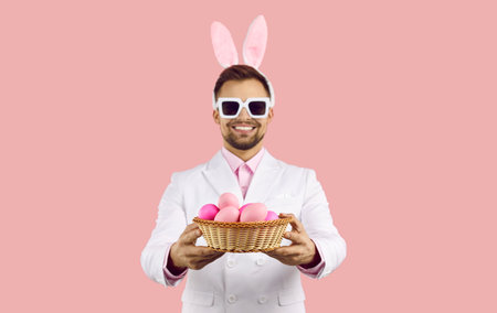 Happy Easter. Cheerful man in ears of Easter bunny, in suit and sunglasses holding basket of Easter...