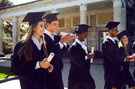 Institute graduates in festive uniforms, in square hats and robes, go forward holding their diplomas...