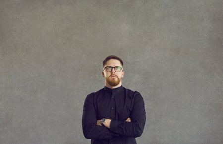 Smart businessman with folded hands on chest thinking looking up standing over studio grey background. Worry pensive man in eyeglasses staring upwards face portrait shot. People emotionの写真素材