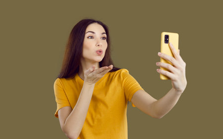 Pretty photo and video blogger blows air kiss and takes selfie on her cellphone. Attractive young...