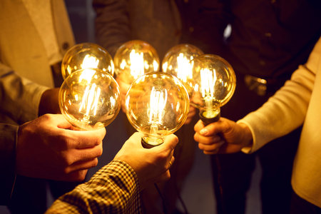 Business team sharing creative energy and developing new ideas. Group of people holding bright glowing electric Edison light bulbs as symbol of idea and innovation. Lightbulbs in human hands, close upの写真素材