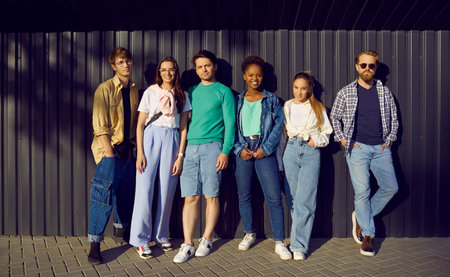 Young people in casual everyday clothes leaning on street wall. Group portrait of six happy relaxed beautiful multiethnic fashion models posing in shirts, tees, jumpers, jeans and denim jacketsの写真素材