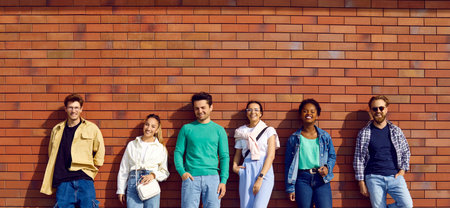 Six diverse relaxed young people in clothes for everyday wear and leisure. Group portrait of handsome men and beautiful women in shirts, tees and jumpers leaning on street wall. Casual fashion conceptの写真素材