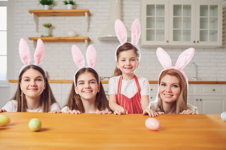 Happy easter. Mother and daughters with rabbit ears decorate Easter eggs sitting at a table in...