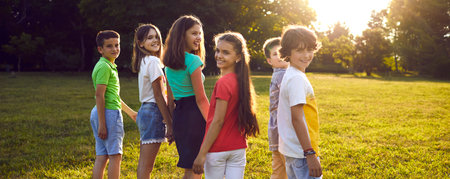 Children friendship. Group of cheerful and cute preteen friends walking together in park on sunny summer day. Smiling boys and girls in casual clothes having fun outdoors. Panoramic web banner.の写真素材