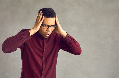 Shocked emotional smart young african american man in eyeglasses looking down toughing head studio shot. Millennial black guy showing impressed omg face feeling surprise, shock and amazementの写真素材