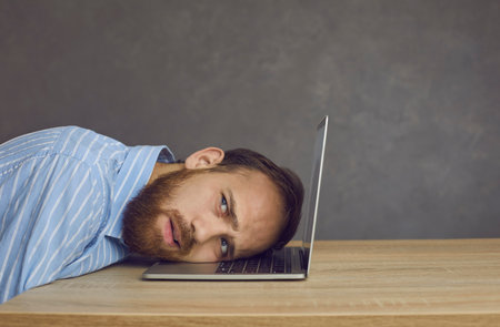 Closeup millennial caucasian sad business man freelancer lying on laptop keyboard with tired grimace on face showing boring facial emotion unable to work. Remote workplace, professional burnoutの写真素材