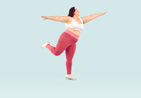 Full length photo of a young smiling fat overweight woman wearing sportswear doing fit exercise isolated on studio blue background. Workout sport, fitness and body positive concept.の写真素材