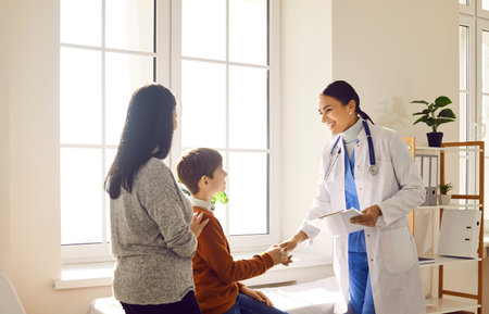 Portrait of a friendly smiling female doctor pediatrician shaking hand with a little boy patient standing with his mother and listening the recommendations after medical examination.の写真素材