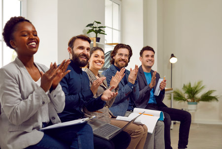 Professional audience applauding the speaker after a good presentation in a business meeting. Group of happy diverse multiethnic people sitting in a row in the office, smiling and clapping handsの写真素材