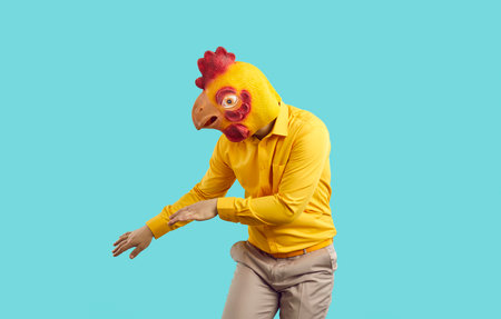 Funny crazy man with chicken head dancing isolated on pastel light blue background. Man in absurd rubber mask of chicken head has fun during costume party. Creative advertising concept.の写真素材