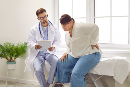 Fat young plump overweight woman sitting on the couch at the medical examination in the doctors office suffering from backache. Obesity problems, rheumatism and healthcare concept.の写真素材