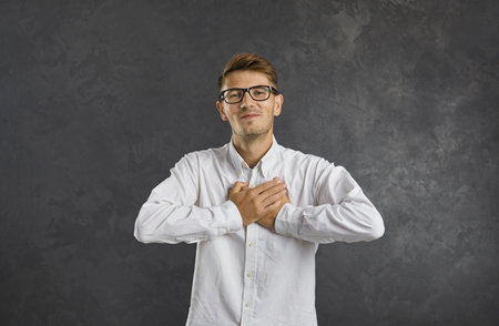 Portrait of happy millennial gen z man on black studio background keep hands on heart chest show gratitude. Smiling young Caucasian male feel grateful thankful send love. Charity, volunteer concept.の写真素材