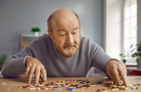 Senior man with Alzheimers disease doing puzzles and other brain training activities. Old bald bearded man with dementia sitting at desk, playing with alphabet, trying to make up words with lettersの写真素材