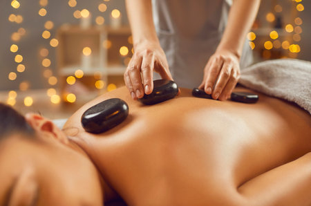 Young woman having hot stone massage in spa salon. Cropped shot of relaxed girl lying on massage bed receiving massage and relaxing. Beauty, treatment therapy, health and healingの写真素材