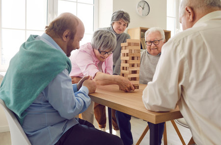 Group of senior people having fun and playing board game in retirement home. Several retired old men...
