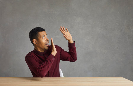 Studio shot of scared dissatisfied african american man stretching hands in refusal gesture sitting...