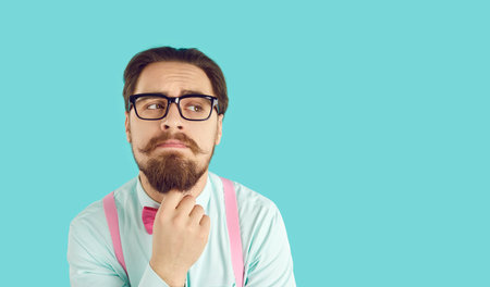 Funny and stylish male nerd thinking or making decisions on light blue background. Guy with mustache...