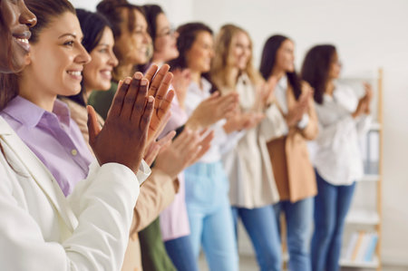 Close up photo of a group of women standing in a row in office and applouding on a meeting or seminar. Female multinational company employees clapping hands at the conference. Selective focus.の写真素材