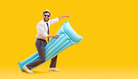 Funny bearded man wearing office clothes with shirt and tie holding inflatable mattress and having fun isolated on yellow background. Happy tourist is going on summer holiday trip. Vacation concept.の写真素材