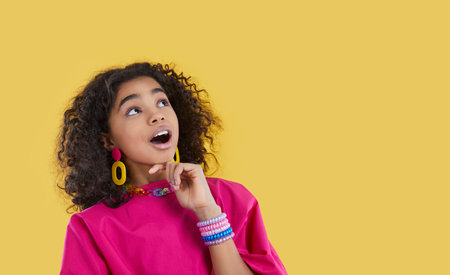 Funny ethnic preteen girl with omg facial expression looks at copy space on yellow background....