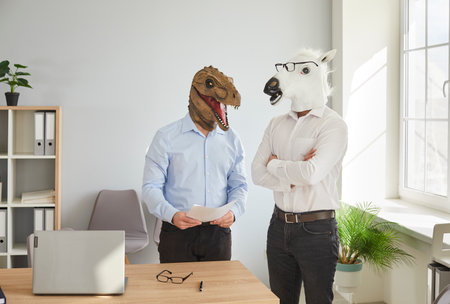 Two funny business men wearing animal masks and shirts standing in office near workplace with financial report or documents and discussing new projects, analyzing company on a meeting.の写真素材