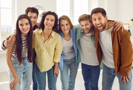 Group of happy smiling funny friends students or colleagues in casual clothes standing together, laughing and looking cheerful and positively at the camera. Friendly guys and girls hugging indoors.の写真素材