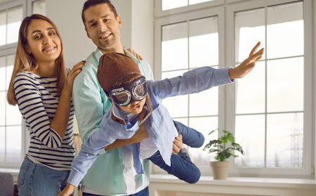 Happy family with child playing and having fun at home. Father holding little son who is pretending to fly like an airplane. Happy little boy in pilot hat and goggles playing with his parents at homeの写真素材