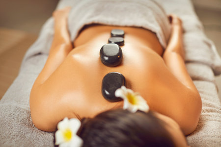 Unrecognizable young man lying on a spa bed, relaxing, getting beauty treatments, and enjoying an exotic back massage with hot stones. Spa treatment, body relaxation, skin care conceptの写真素材