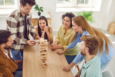 Top view portrait of a group of happy young friends students guys and girls playing together in board game with wooden building blocks at home and enjoying time together sitting at the table.の写真素材