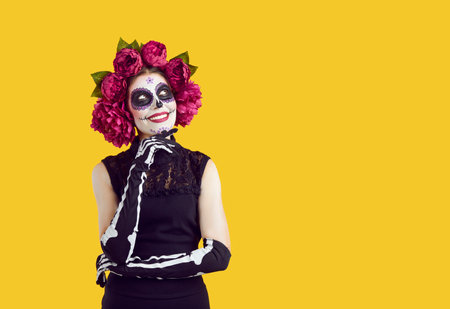 Portrait of happy woman with sugar skull makeup, skeleton gloves and flowers on head smiling...