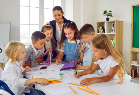 Group concentrated children boys and girls with woman teacher solve tasks together or draw standing...