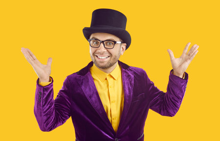 Entertainer presents new holiday circus show program. Man wearing purple velvet suit and tophat spreads hands, smiles and looks at camera with happy funny face expression isolated on yellow backgroundの写真素材