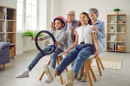 Happy grandparents and children play games together. Funny grandfather, grandmother, little girl, and boy in helmet with steering wheel sit on chairs, imagine to be in car and pretend to drive awayの写真素材