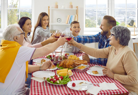 Family toast. Joyful friendly multigenerational family clinking wine glasses during Thanksgiving celebration. Family members of different ages are sitting together at home at festive table.の写真素材