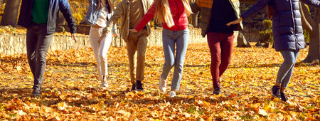 Legs and shoes of young people walking in park. Cropped shot of men and women wearing warm casual clothes and sneakers walking outdoors together in autumn sunny dayの写真素材