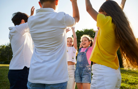 Happy children friends standing together outdoor in summer park raising their hands up enjoying meeting on holidays spending time in a summer camp. Portrait of kids having weekend activity.の写真素材